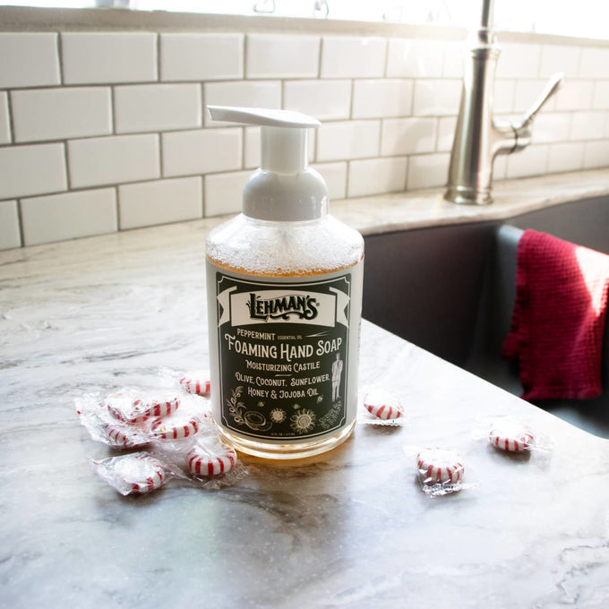 Handcrafted Lehman's foaming hand soap with peppermint scent and natural moisturizing oils like olive, coconut, sunflower, honey, and jojoba on a kitchen counter near peppermint candies, ideal for Health & Wellness and Grooming collections.