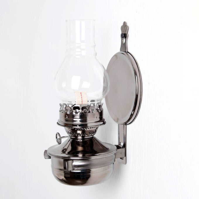 Wall-mounted oil lamp with a pewter-like finish, clear ribbed glass chimney, and round reflector, designed for warm, ambient lighting in lamps & lighting and oil lamps collections.