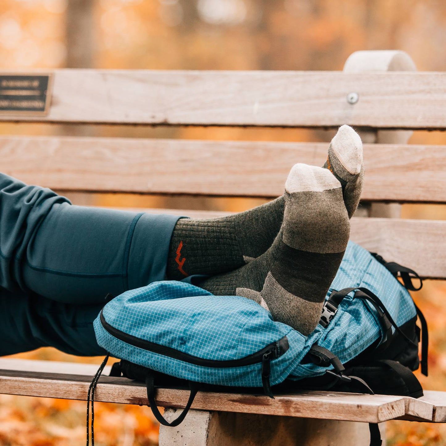 Men’s midweight hiking socks in earth tones resting on a blue backpack on a wooden bench, perfect for camping, outdoor activities, and USA made collections at Lehman’s.