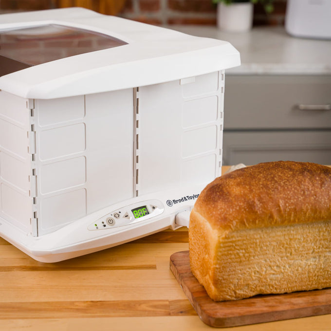 White folding bread proofer with digital display showing rising mode next to a freshly baked loaf on a wooden cutting board, featured in Kitchen & Food and Baking Supplies collections.