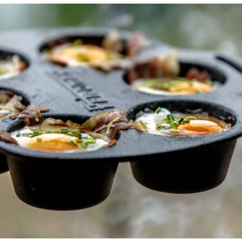 Close-up of cast iron muffin pan cooking eggs wrapped with bacon and garnished with herbs, showcasing durable cookware ideal for camping, kitchen, and outdoor use in cast iron and cookware collections.