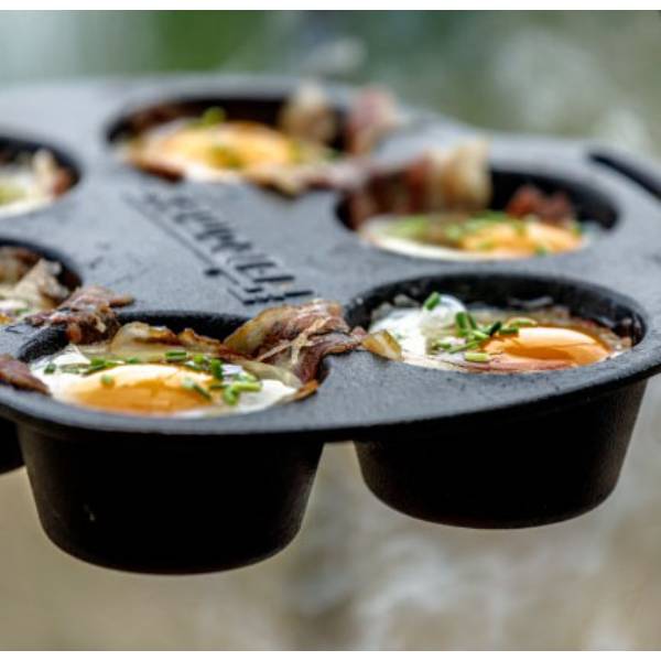 Close-up of cast iron muffin pan cooking eggs wrapped with bacon and garnished with herbs, showcasing durable cookware ideal for camping, kitchen, and outdoor use in cast iron and cookware collections.
