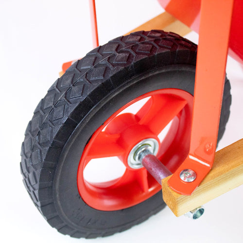 Close-up of a rugged rubber tire with deep tread on a child's wheelbarrow featuring sturdy wood handles and a bright red metal frame, part of Toys, Books & Games and Lawn Games collections.