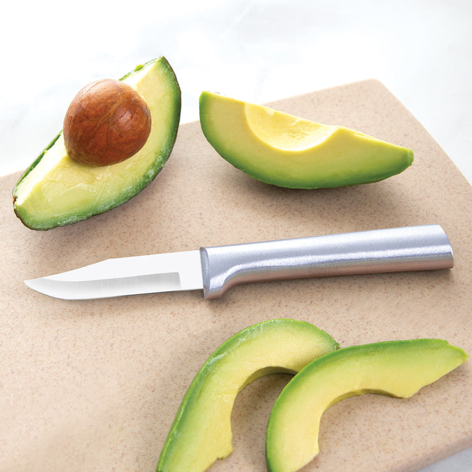 Sharp carbon stainless steel paring knife with a satin-finished cast aluminum handle lying on a cutting board next to fresh avocado slices in a kitchen food prep setting, ideal for USA made collections.