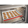 Flexible red silicone oven rack guard installed on the front edge of a metal oven rack with a baking sheet of freshly baked chocolate chip cookies inside, enhancing kitchen safety in Best Sellers and Kitchen Accessories collections.