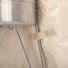 Close-up of beige ripstop fabric with a fastening strap secured beside a metal fire barrel leg, showcasing durable weatherproof protection designed for outdoor Farm, Garden & Tool and Camping use.