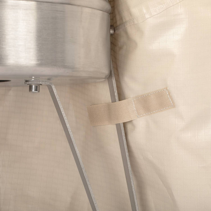 Close-up of beige ripstop fabric with a fastening strap secured beside a metal fire barrel leg, showcasing durable weatherproof protection designed for outdoor Farm, Garden & Tool and Camping use.
