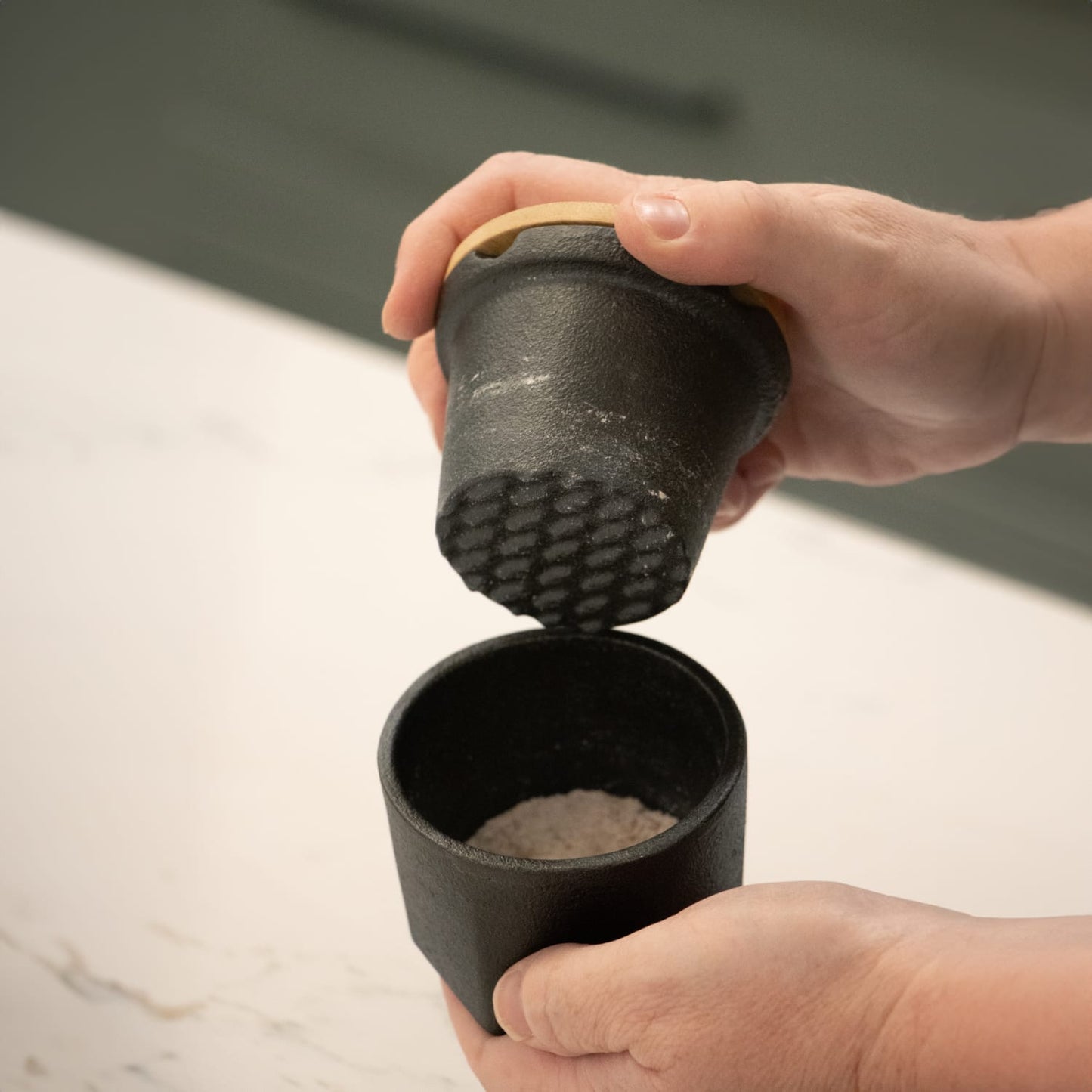 Handheld cast iron spice grinder with bamboo lid and silicone gasket, shown grinding spices over matching cast iron cup, part of Kitchen & Food and Kitchen Gadgets collections.
