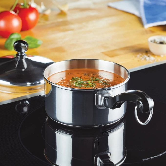 Stainless steel 1-quart saucepan with black handle filled with tomato soup garnished with herbs, placed on a black stovetop in a kitchen setting, featured in Kitchen & Food and Cookware collections.