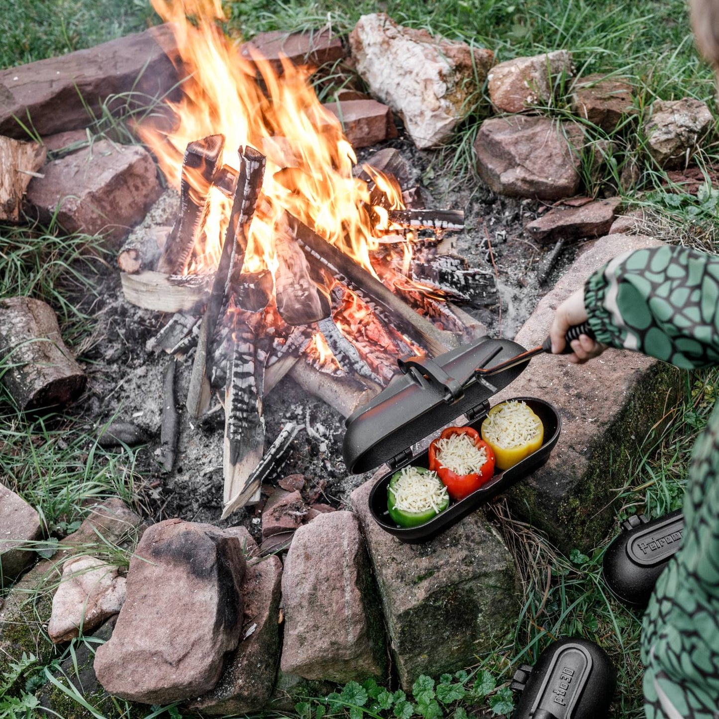 Cast iron potato cooker with hinged lid cooking stuffed bell peppers over an open campfire, ideal for Farm, Garden & Tool, Camping, Best Sellers, and Promo Eligible collections.