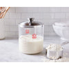 Clear borosilicate glass crock with stainless steel lid holding sourdough starter beside a metal measuring cup filled with flour, perfect for Kitchen & Food, Baking Supplies, and Cookware collections.