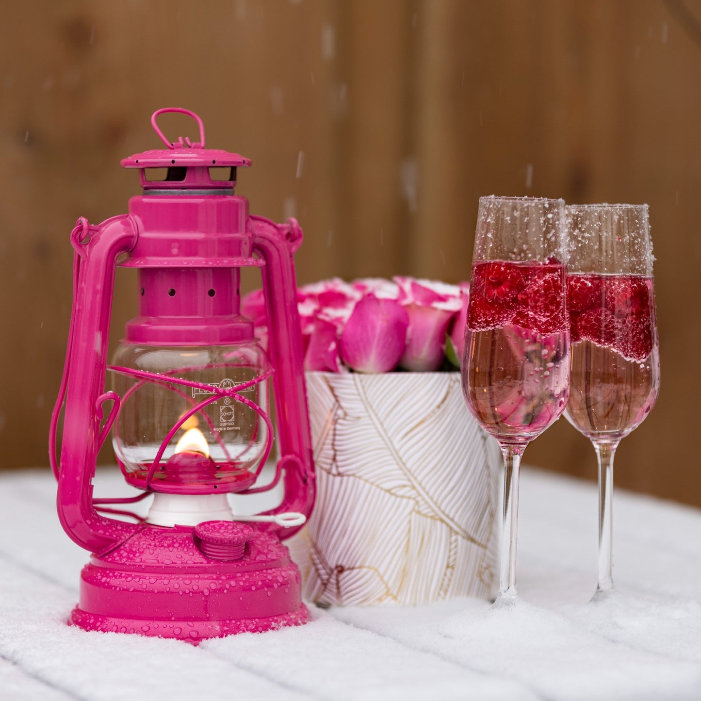 Handcrafted bright pink galvanized oil lantern with thermal heat-resistant globe glowing warmly beside a floral arrangement and two sparkling rose wine glasses, ideal for Camping, Lamps & Lighting, and Emergency Supplies collections.