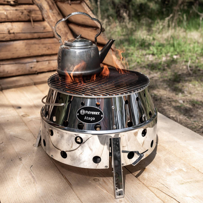 Petromax stainless steel teakettle heating on a polished metal portable fire pit grill outdoors, ideal for Farm, Garden & Tool, Kitchen & Food, Camping, Brewing Coffee and Tea, and Best Sellers collections.