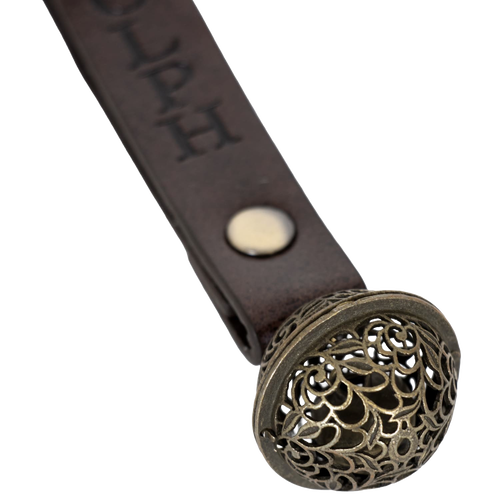 Close-up of a handcrafted antique-style brass bell with a filigree pattern, attached to a brown leather strap engraved with a reindeer's name, for Home & Decor, Holiday Decor, Best Sellers, Promo Eligible, Sale collections.