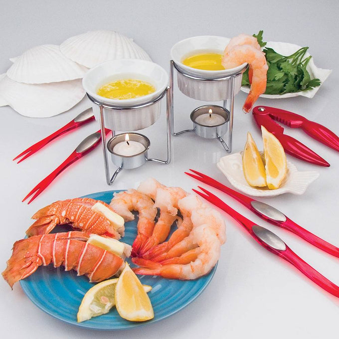 Set of 2 white ceramic butter warmers on metal stands with lit tealights beneath, surrounded by shrimp, lobster, lemon wedges, red seafood forks, and shell-shaped serving dishes in Kitchen & Food and Storage and Serving collections.