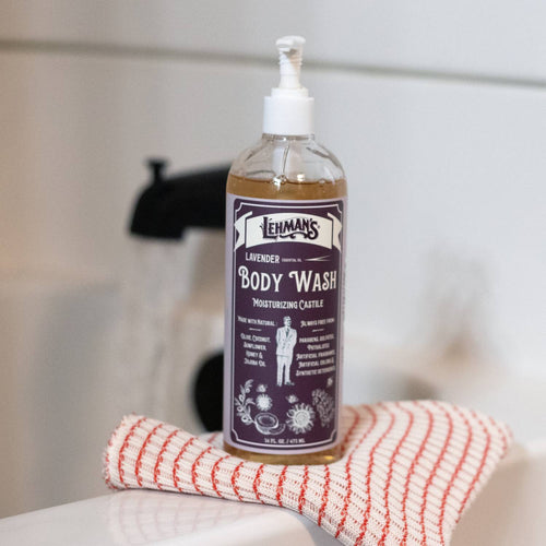 Handcrafted bottle of Lehman's moisturizing castile body wash in lavender scent, featuring natural ingredients like olive and jojoba oils, placed on a textured towel in a bathroom setting.