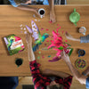 People assembling a 300-piece shaped hummingbird jigsaw puzzle with vibrant colors on a wooden table, surrounded by mugs, a teapot, and snacks, ideal for Toys, Books & Games collections.