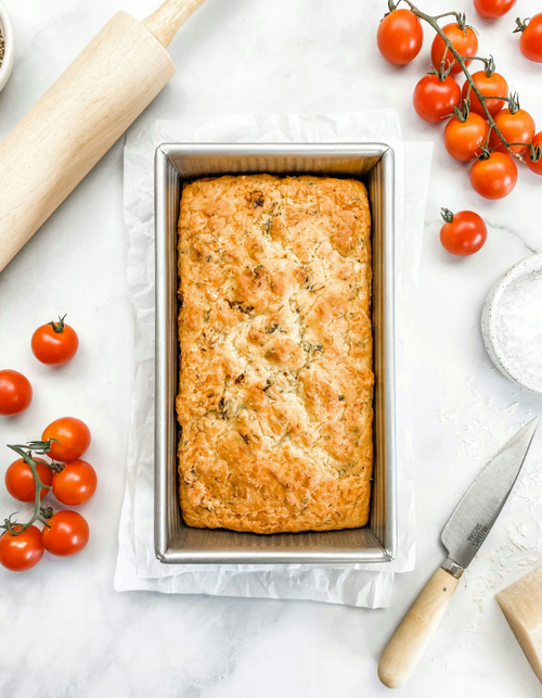 Handcrafted nonstick aluminized steel loaf pan with freshly baked golden bread, surrounded by cherry tomatoes, a rolling pin, and a knife, featured in Kitchen & Food and Bakeware collections.