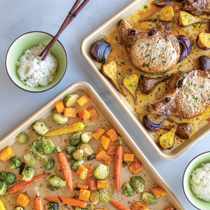 Two nonstick half-sheet pans made of aluminum with roasted pork chops, squash, mushrooms, and onions on one pan, and assorted roasted vegetables on the other, alongside bowls of rice with chopsticks, featured in Kitchen & Food, Cookware, Baking Supplies, Pots and Pans, USA Made, Best Sellers, and Promo Eligible collections.