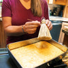 Person holding a handcrafted Amish-style broom cake tester with a metal loop, poised to poke a straw into a freshly baked sheet cake in a kitchen, featured in Kitchen & Food and USA Made collections.