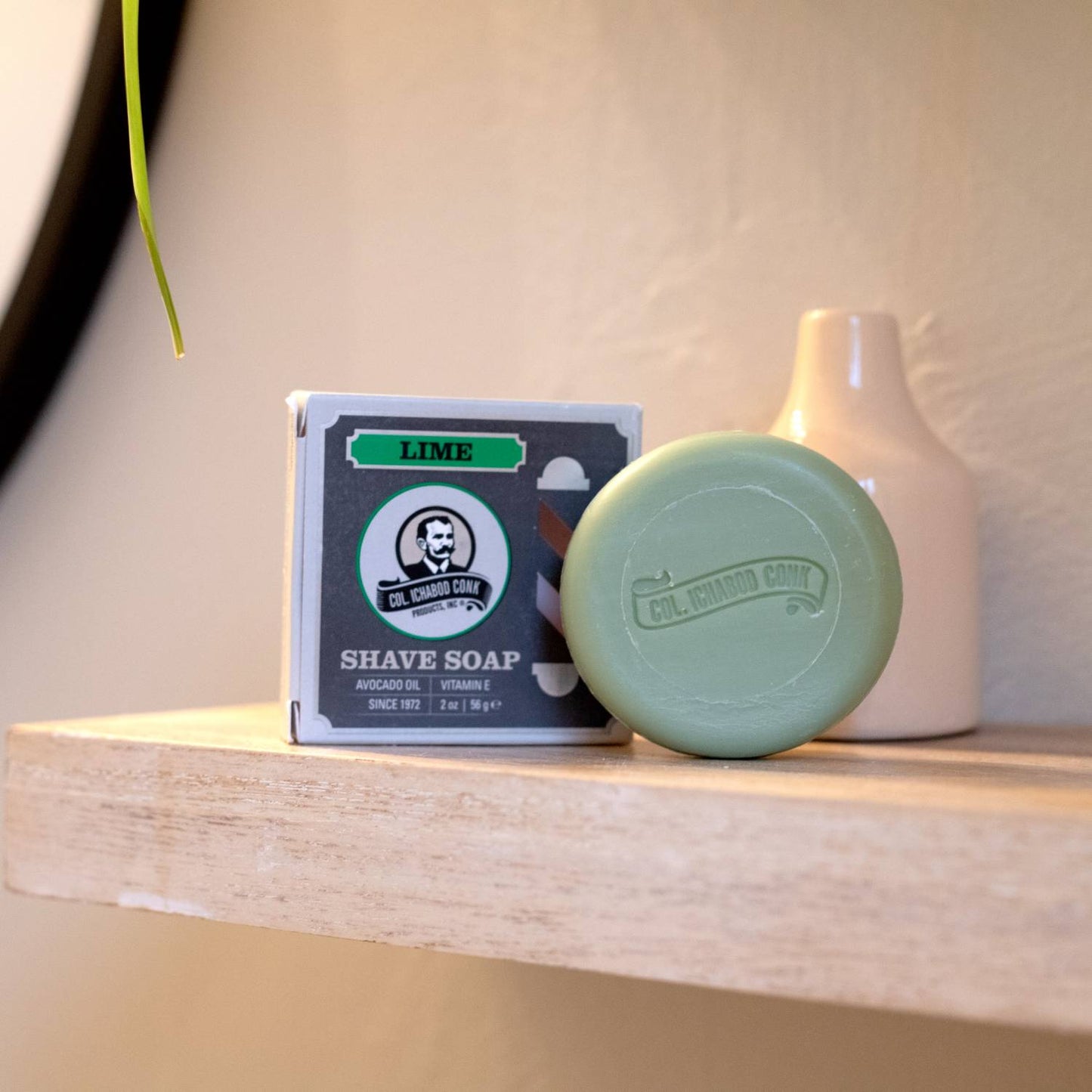 Round lime green shaving soap bar embossed with brand logo next to its boxed packaging, styled on a wooden shelf with neutral background, featured in Health & Wellness, Grooming and Personal Hygiene, Soaps and Soapmaking, USA Made, Best Sellers, Promo Eligible collections.