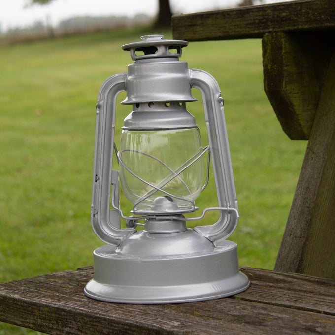 Handcrafted silver metal lantern with clear glass globe and protective wire cage, designed for dependable lighting in farm, garden, camping, emergency supplies, and outdoor settings.