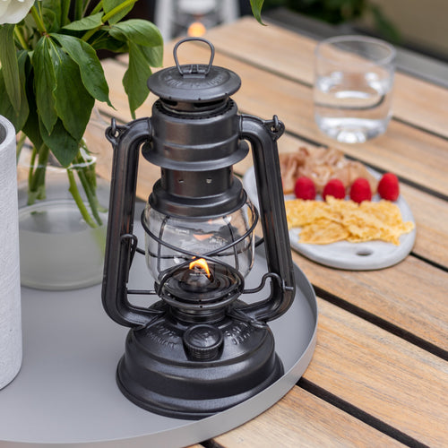 Handcrafted black galvanized lantern with thermal heat-resistant globe glowing gently on a round tray beside fresh greenery and a snack plate, perfect for Camping, Lamps & Lighting, and Emergency Supplies collections.