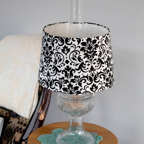 Black and white damask pattern cloth lamp shade designed for Aladdin oil lamps, shown on a clear glass lamp base in a cozy home setting, part of Lamps & Lighting collections.