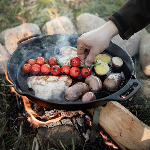 Cast iron skillet with two side handles cooking cherry tomatoes on the vine, potatoes, mushrooms, and meat over an open campfire, perfect for farm, garden, kitchen, camping, cookware, and cast iron collections.