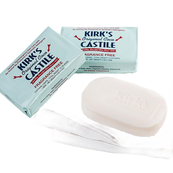 Three-pack of fragrance-free bar soaps in light blue wrappers and one unwrapped creamy white bar resting on a white cloth, made in USA for sensitive skin in Health & Wellness and Grooming collections.