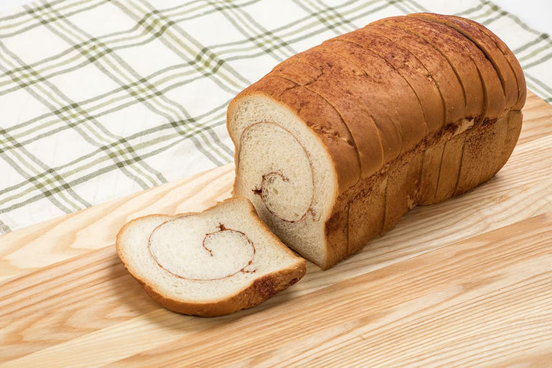Sliced handmade cinnamon bread loaf with a soft texture and a cinnamon swirl, presented on a wooden board over a plaid cloth, ideal for Kitchen & Food and USA Made collections.