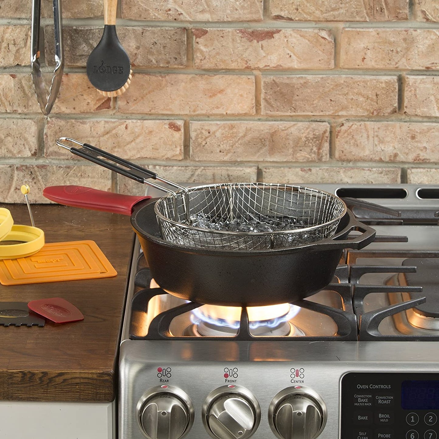 Black cast iron deep skillet with assist handle and long grip on gas stove burner, holding a wire frying basket, featured for versatile cooking in Farm, Garden & Tool, Kitchen & Food, Camping, Cookware, Cast Iron, Best Sellers, and Promo Eligible collections.