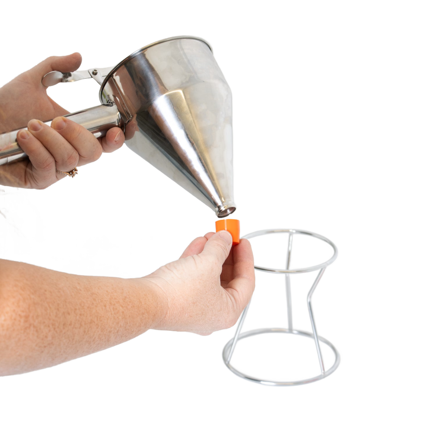 Person holding a stainless steel batter dispenser with thumb lever, attaching an interchangeable orange silicone tip above a white metal stand, part of Kitchen & Food and Cookware collections.