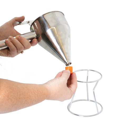 Person holding a stainless steel batter dispenser with thumb lever, attaching an interchangeable orange silicone tip above a white metal stand, part of Kitchen & Food and Cookware collections.