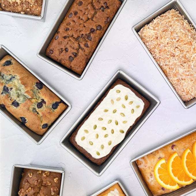 Collection of large loaf pans made from durable recycled steel, each filled with different baked goods including frosted, nut-topped, and fruit-adorned breads, ideal for Kitchen & Food and Baking Supplies collections.