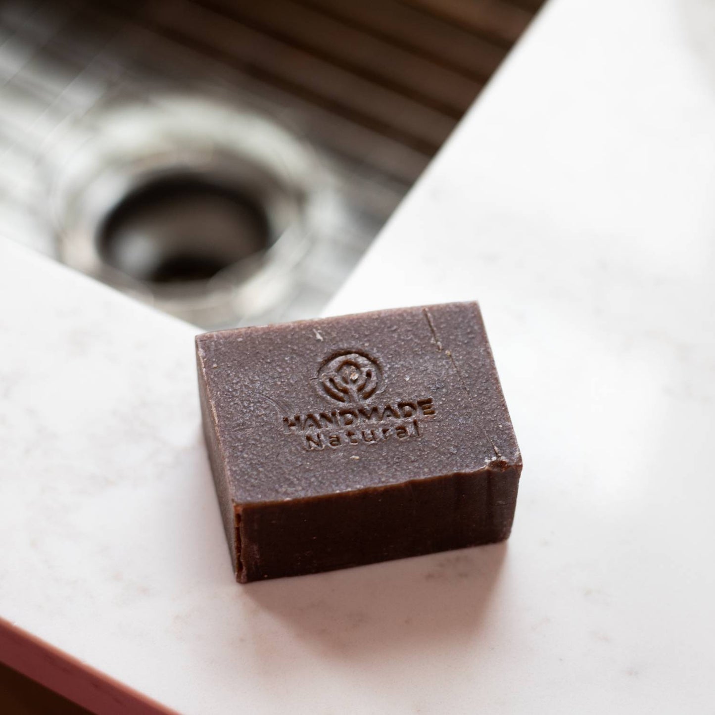 Handcrafted chemical-free natural dish bar soap with embossed logo, resting on a white kitchen countertop near a stainless steel sink, featured in Home & Decor and Household Cleaning collections.