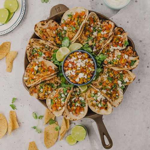 Handcrafted cast iron skillet filled with vibrant chicken tacos topped with fresh vegetables and cheese, garnished with lime wedges and surrounded by tortilla chips, ideal for Kitchen & Food, Cookware, Cast Iron, USA Made, Camping, and Farm, Garden & Tool collections.