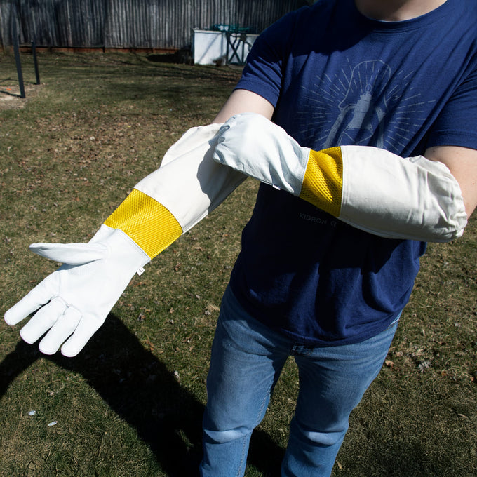 Person wearing smooth white goatskin beekeeping gloves with yellow vented cuffs and elastic wrists, designed for protection and dexterity in farm, garden, and beekeeping tasks.