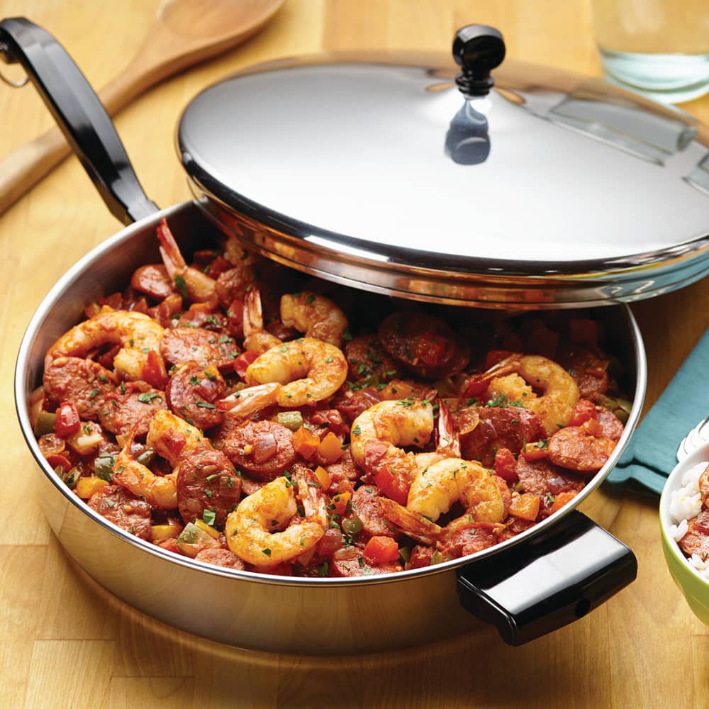 Stainless steel covered fry pan filled with seasoned shrimp and sausage dish, shown on wooden surface with spoon and glass, perfect for Kitchen & Food, Cookware, Pots and Pans collections.