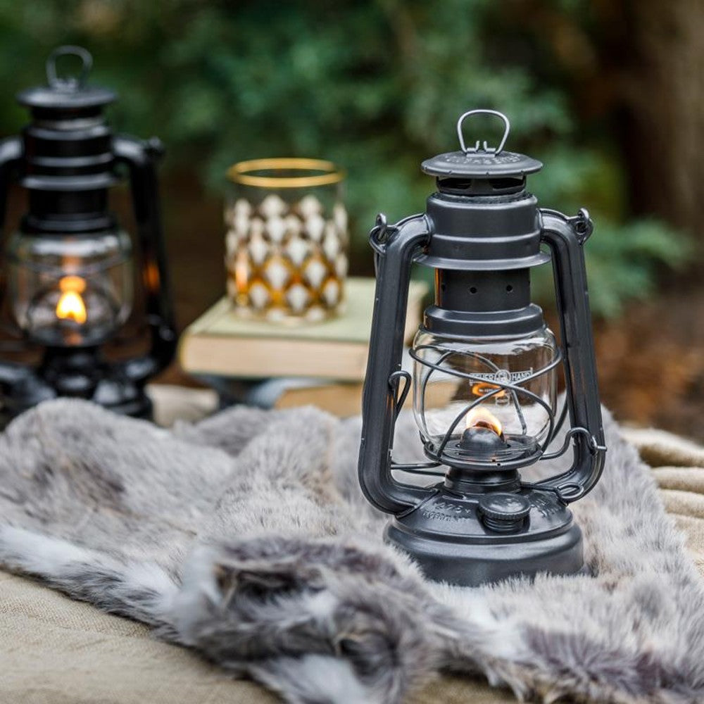 Handcrafted black galvanized oil lantern with thermal heat-resistant globe softly glowing outdoors on a rustic fur throw, perfect for Lamps & Lighting, Camping, and Emergency Supplies collections.