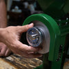 Hand adjusting the fineness setting on a sturdy green grain mill with stainless steel burrs, designed for homesteading, kitchen, and emergency food grinding needs.