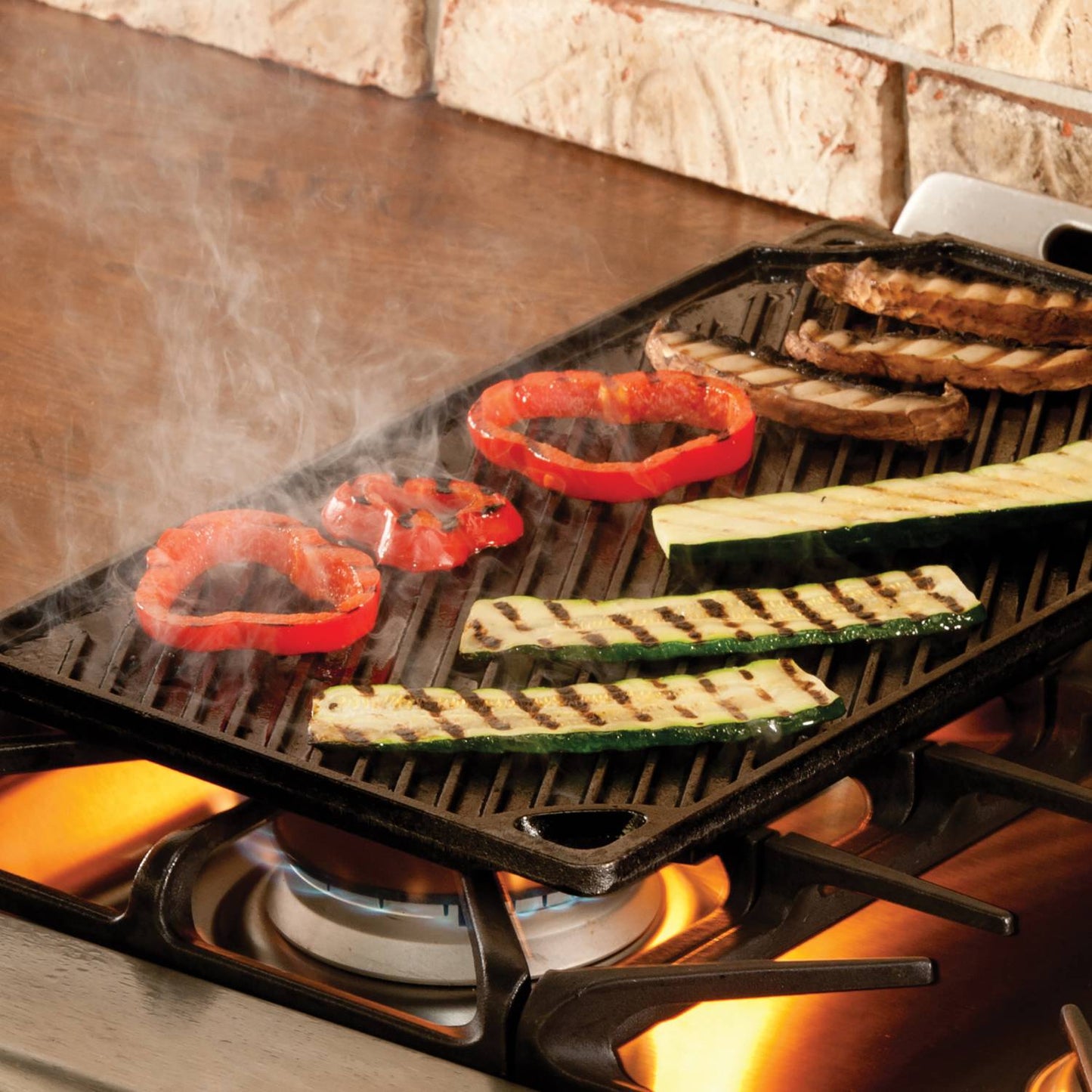 Reversible cast iron griddle with ribbed grilling surface cooking red bell peppers, zucchini strips, and mushrooms over a gas stove burner, part of USA Made kitchen cookware collections.