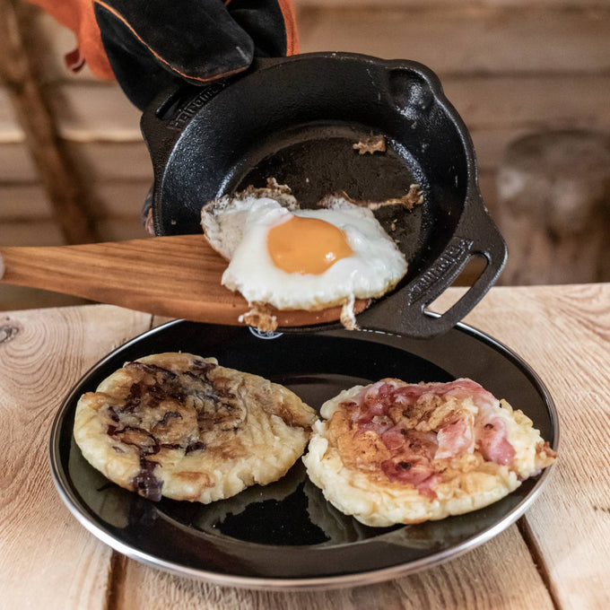 Cast iron fire skillet with two side handles being used to cook a fried egg, showcasing durable cookware for Farm, Garden & Tool, Kitchen & Food, Camping, and Cast Iron collections.