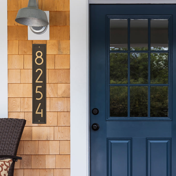 Handcrafted vertical custom address plaque in aged bronze with contemporary numbers mounted on natural wood siding by a blue front door, enhancing curb appeal in Home & Decor, Household Helpers, Mailboxes and Address Signs, USA Made, and Best Sellers collections.