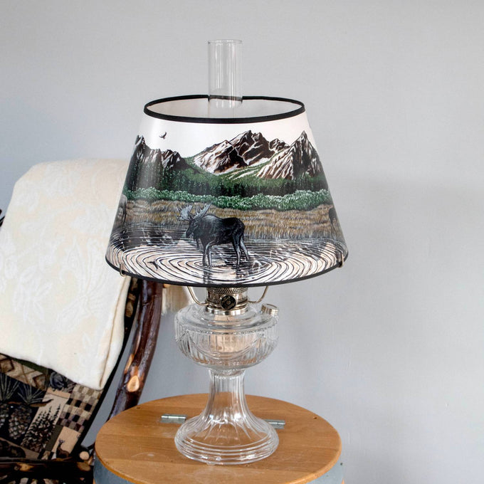 Clear glass oil lamp with a decorative Rocky Mountain High parchment shade featuring a moose by a lake and forest scene, ideal for Lamps & Lighting, Oil Lamps, Table Lamps, Best Sellers, and Promo Eligible collections.