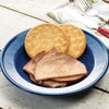 Blue enamelware plate holding several slices of smoked ham alongside round saltine crackers on a rustic white wooden surface, suitable for Farm, Garden & Tool, Kitchen & Food, Emergency Supplies, Freeze Dried, and USA Made collections.