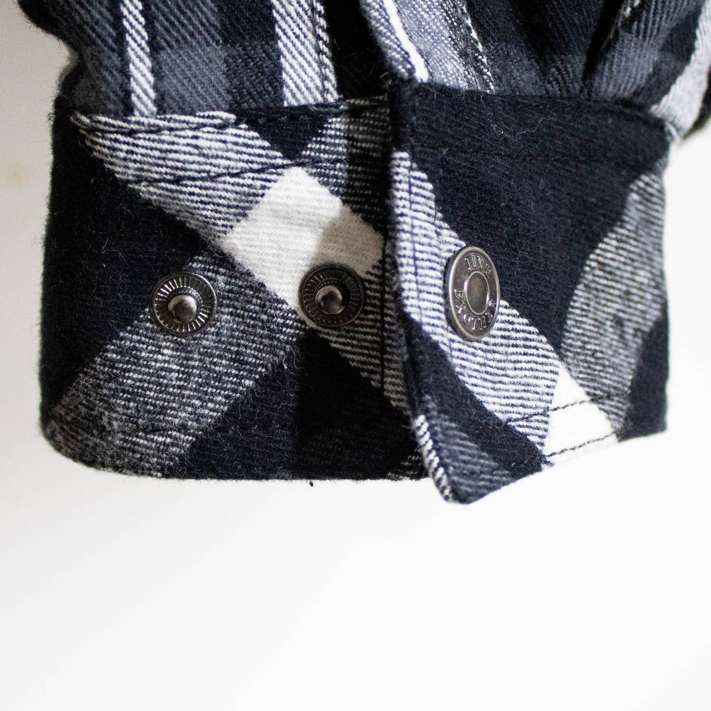 Close-up of a handcrafted black and white plaid flannel cuff with detailed woven texture and metal snap buttons, featured in Health & Wellness and Clothing and Accessories collections.