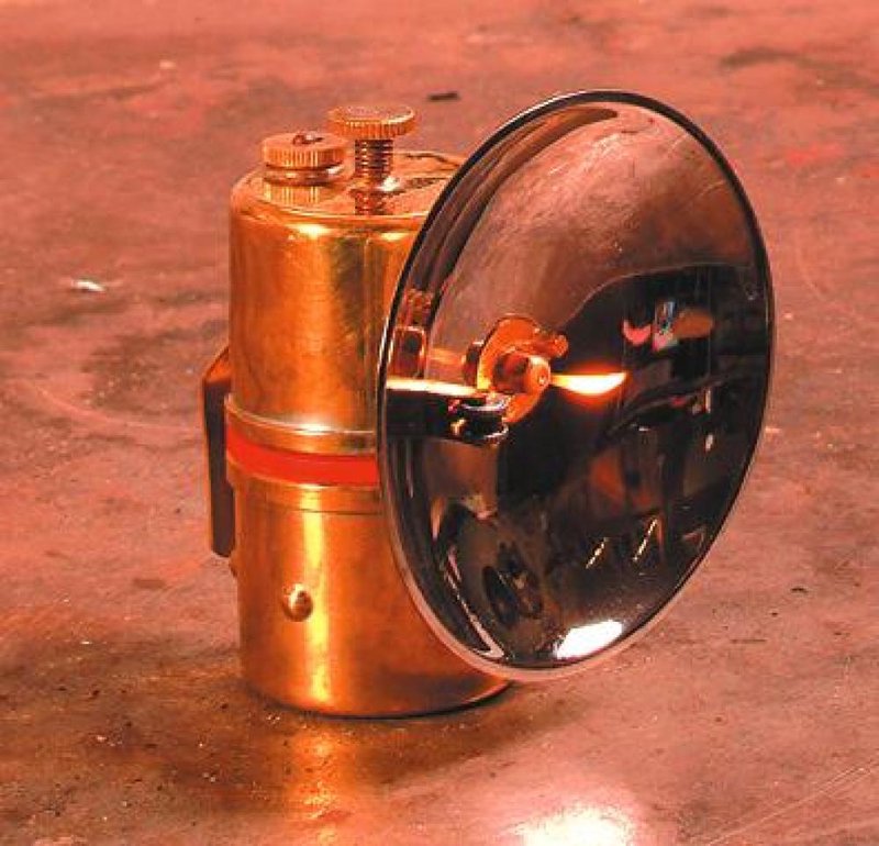 Solid brass carbide lamp with polished reflector and flint striker, handcrafted for reliable white light, ideal for camping, barn, and outdoor use in lamps and lighting collections.