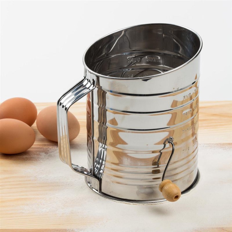 Shiny stainless steel flour sifter with a wooden handle crank, designed for precise baking, shown on a wooden surface with eggs nearby, part of Kitchen & Food and Baking Supplies collections.