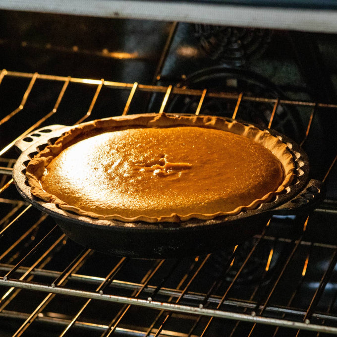 Handcrafted cast iron pie pan with crimped edges baking a golden pie in the oven, showcasing even heat retention for Kitchen & Food, Cookware, Cast Iron, Baking Supplies, and Best Sellers collections.